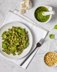 Green fussili pasta made of mungo beans with vegan homemade basil pesto and herbs. Italian pasta. Italian food. Home made food. Concept for a tasty and healthy meal. Gray stone background. Top view.