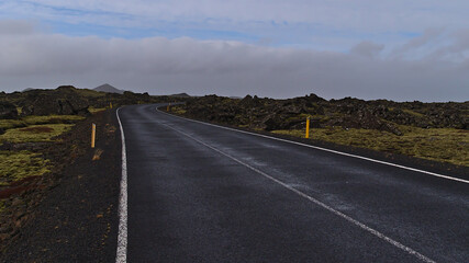 Diminishing perspective of winding country road with markings between moss covered lava fields of volcanic stones near Grindavik, Reykjanes peninsulsa, Iceland on cloudy winter day.