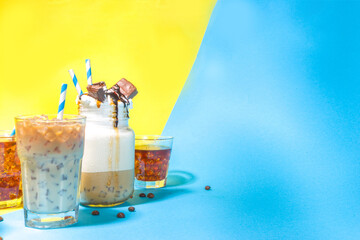 Set with different iced summer coffee drinks - espresso, frappe, latte, cappuccino, with whipped cream, syrup and crushed ice, in various glasses and mugs on trendy bright yellow blue background