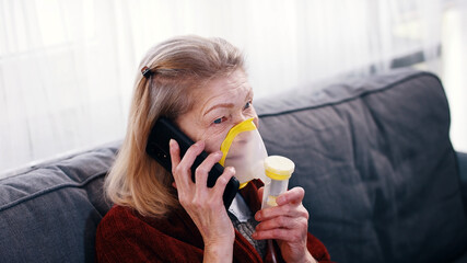 Elderly woman using oxygen inhaler while speaking on the phone. Coronavirus outbreak and vulnerable...