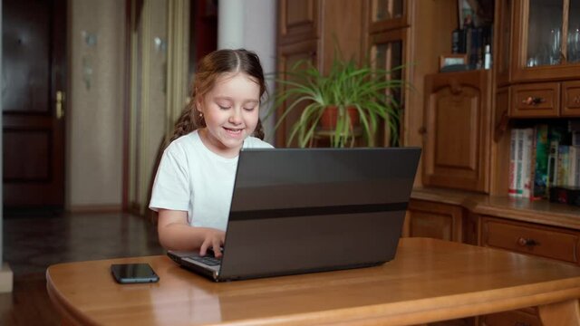 A little cute girl looks at the laptop screen and is excited by luck and success, maybe she won the game or the lottery. Concept of a winner in cyberspace and training for the ps. Child at home indoor
