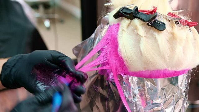 The hairdresser dyes the hair of a blonde woman in different bright colors