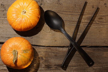 Two pumpkins and a black spoon with tongs on a wooden table