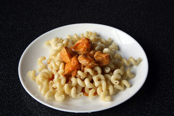 Pasta with chicken in tomato sauce on a white plate. Chicken goulash with garnish.