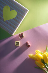 Green and pink chocolate candy next to a bouquet of yellow tulips on a bright background
