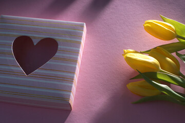 Bouquet of yellow tulips on a pink background and a box with a heart