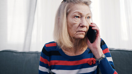 Elderly woman using smartphone to make phone call. Receiving bad news. High quality photo