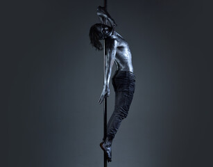 Art sexy man body. Performance concept. Man with nude torso covered with silver paint. Guy hanging on metallis pole. Athlete, sportsman performing pole dancing moves, work out, show trick.