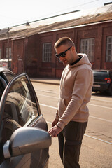 A young man next to his car on a sunny day on the street of the old city.