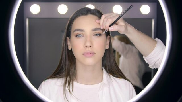 Reflection in a mirror of a caucasian female model applying eyes makeup. Make-up artist uses a makeup brush while prepare a model for a show. High quality 4k footage