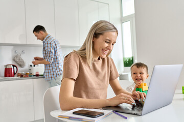 Happy young mom business woman distance working online using laptop computer while small funny kid son playing having fun sit at kitchen table. Virtual homeoffice work and child care in family life.