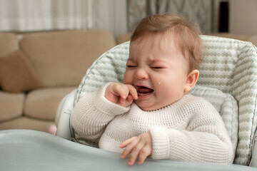 Baby boy sitting in a feeding chair and crying. Real people in real interior. 