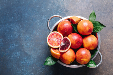 Whole and sliced blood oranges in iron bowl colander on blue table background. Flat lay, top view,...