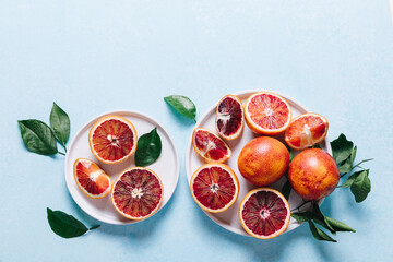 Composition of whole and sliced blood oranges in a plate on light blue table background. Flat lay,...