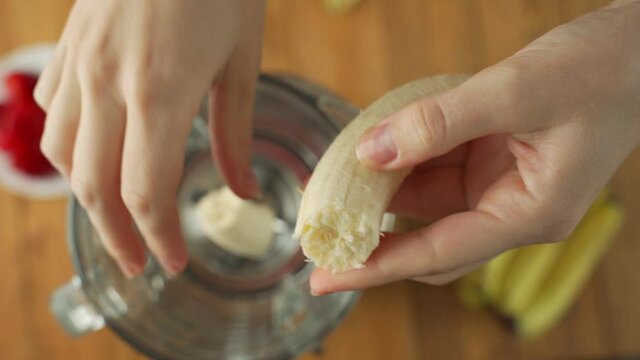 Hand adds fresh banana in a blender to prepare healthy vegan fruit smoothie