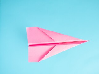 A pink paper airplane on a light blue bright background. Minimal flat lay travel concept.