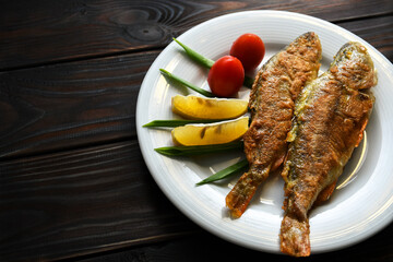Fried fish on a plate with vegetables, lemon and onion