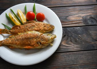 Fried fish on a plate with vegetables, lemon and onion