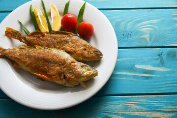 Fried fish on a plate with vegetables, lemon and onion