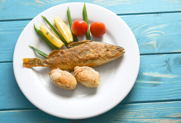 Fried fish on a plate with vegetables, lemon and onion