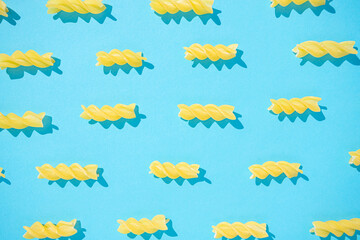A pattern made of pieces of pasta in the shape of screws on a light blue background. Flat lay creative arrangement.