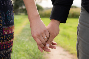 couple holding hands, close up she has an engagement ring on her finger in the foreground with an...