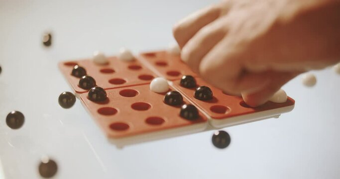 Board game with black and white balls on the red playing field, white background. Mans hand makind step and turning part of the field