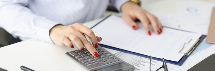 Business woman with red manicure counting on calculator in office closeup