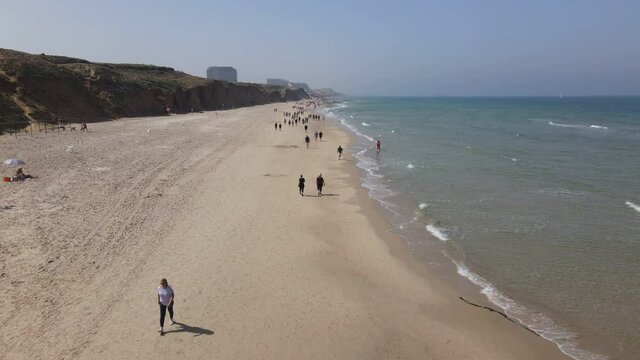 Herzliya, Israel - April 18, 2021: locals walk, Mediterranean coast, beach from the pier. Tide of waves of seawater, coastal sand. Resort hotel by the sea. The embankment