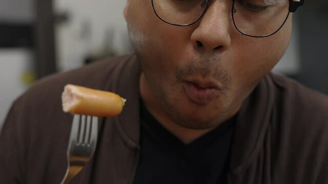 A young Asian man eating breakfast, he eats pork sausage. He poked it with a fork and bit his gut and chewed deliciously. Slow motion and movement short