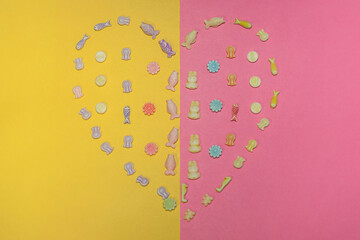 Shape heart made with plastic charms on yellow and pink background