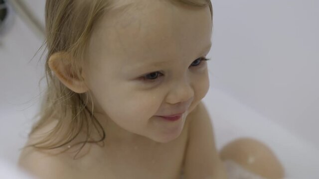 Attractive 2 year old girl takes a bath. Wet hair. Cute blonde child. Pretty little toddler in bathroom. Positive emotions. Pediatrics concept. Happiness in childs eyes. Entertainment and leisure