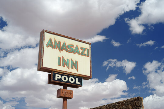 This image shows a vintage sign of an abandoned motel against a blue sky and clouds.