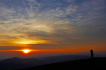 Fototapeta na wymiar lonely traveler high in mountains photographs sunrise or sunset in trip