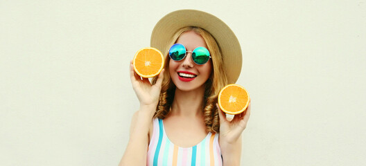 Summer portrait of happy smiling young woman with slices of orange wearing a straw hat, sunglasses on a white background