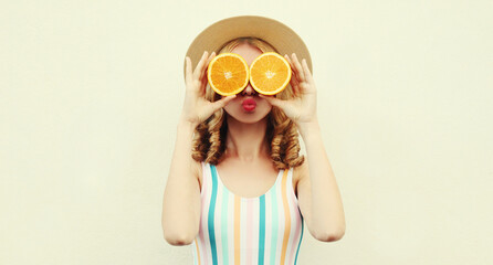 Summer positive portrait of cheerful woman covering her eyes with slices of orange looking for something wearing a straw hat on a white background