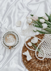 White tulips, coffee cup and woman accessory on silk background,  Morning coffee cup spring mood. Luxury romantic background. Woman morning, aesthetic concept. Top view, flat lay