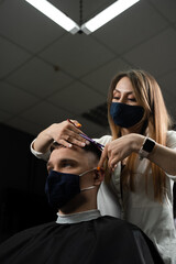 Fototapeta na wymiar Barbershop service at coronavirus covid-19 period. Woman barber making hair for handsome man. Using mask.