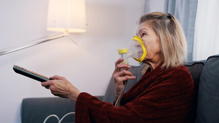 Elderly woman using oxygen mask while changing channels on tv at home. High quality photo