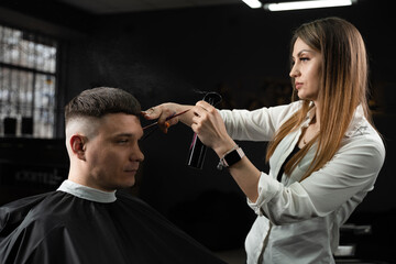 Woman barber making hairstyle in barbershop using clipper. Hairdresser cutting hair of handsome man.