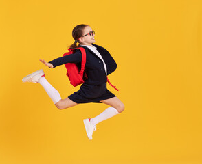 Fototapeta na wymiar Excited schoolgirl jumping high in studio