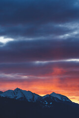 Alpine mountains with snow tops at sunset with dramatic red colored stormy cloudscape in Tirol, Austria