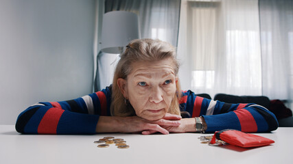 Desperate old woman pensioner looking at small amount of coins on the table. High quality photo