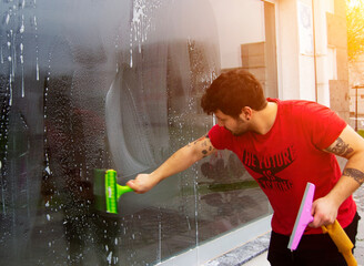 handsome young man in red shirt cleaning window with rag and wiping