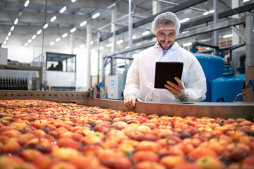 Technologist standing in food processing factory and checking quality of apple fruit.