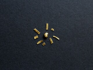 A grain of pure gold 24 karat, precious metal important in business, industry and jewelry, arranged in the shape of a little shiny sun with golden chips as rays around it on black background.