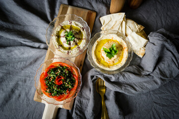 three glas bowls with Taboule salad, hummus and eggplant dipp with brad on grey cloth.