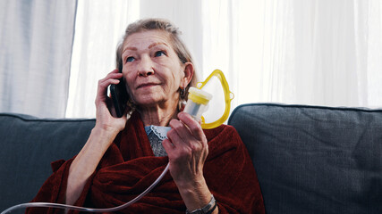 Elderly woman using oxygen inhaler while having a phone call. Vulnerable person during covid...