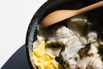 Closeup of wonton soup with seaweed, egg, and dried shrimps in a ceramic bowl isolated on a white background.