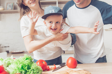 Happy family of mom, son and father are cutting vegetables on salad  and having fun together in kitchen.